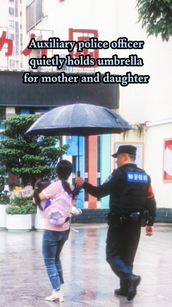 Chinese auxiliary police officer quietly holds umbrella for mother, daughter in rain